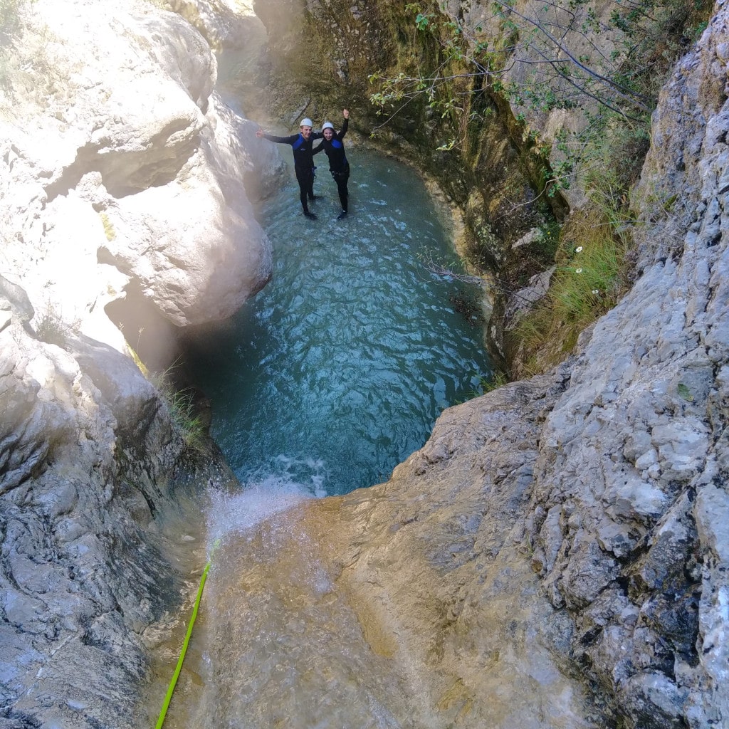 Deux personnes en canyoning dans une rivière turquoise encaissée.