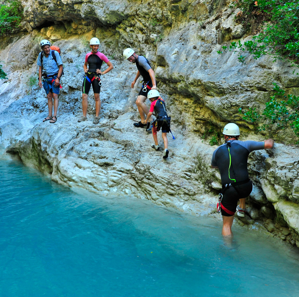 Un groupe de personnes faisant du canyoning dans une rivière turquoise entourée de parois rocheuses.