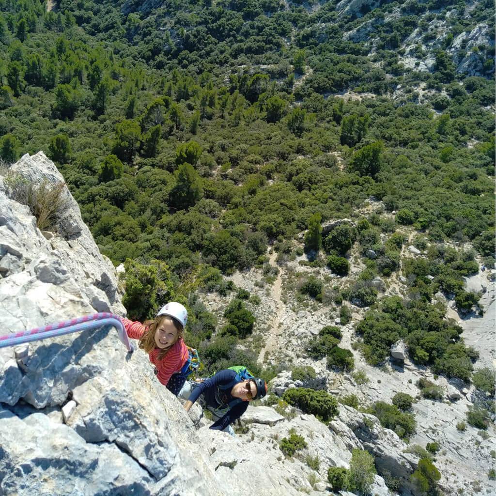 Une vue panoramique d'un paysage forestier dense et verdoyant dans la Drôme. L'image montre une vaste étendue de cimes d'arbres, avec quelques affleurements rocheux visibles au loin ainsi qu'une jeune fille qui escalade.