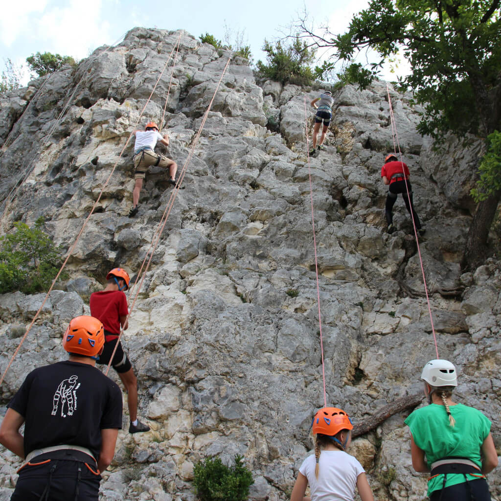 Un groupe de grimpeurs escaladent une falaise rocheuse escarpée dans la Drôme. Ils utilisent des cordes, des harnais et d'autres équipements d'escalade pour naviguer sur ce terrain accidenté.